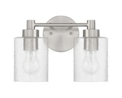 The Lyndsey - 60202 by Craftmade is a modern wall sconce with two clear glass shades and visible bulbs. It showcases a brushed metal finish and an oval mount, offering a sleek, contemporary style.